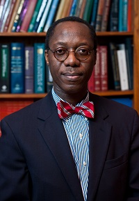 Headshot of Dr. Obisesan wearing a suit and striped bow-tie standing in a library